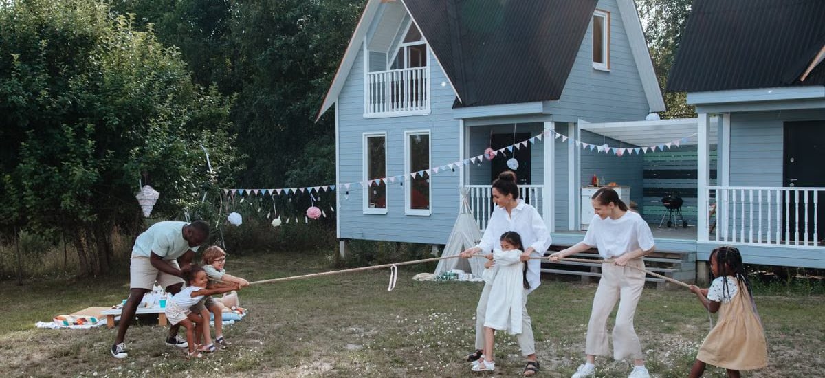Happy family playing tug of war in front of cozy houses during a summer day.