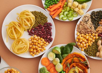 A vibrant mix of legumes, vegetables, nuts, and pasta arranged on white plates showcasing a balanced, healthy diet.